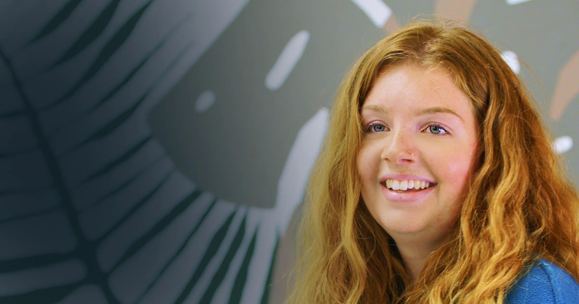 A woman with long red hair and a warm smile looks off-camera. The background features abstract lines and shapes, creating a lively, artistic atmosphere.